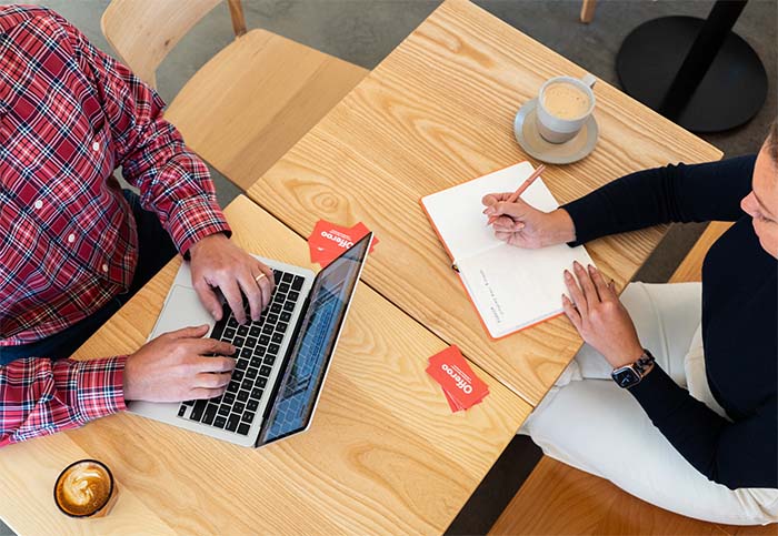 Two people sitting at a table with a laptop and notepad